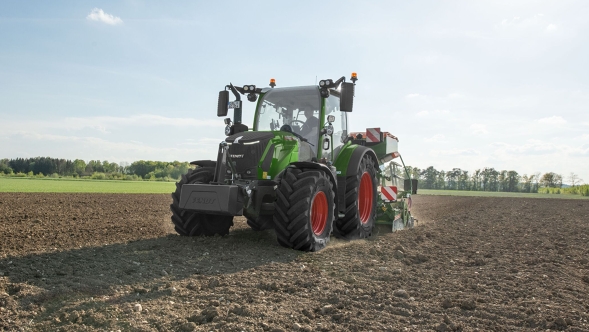 Ein Fendt 300 Vario Gen5 Traktor arbeitet mit einer angebauten Sämaschine auf einem frisch vorbereiteten Acker bei sonnigem Wetter