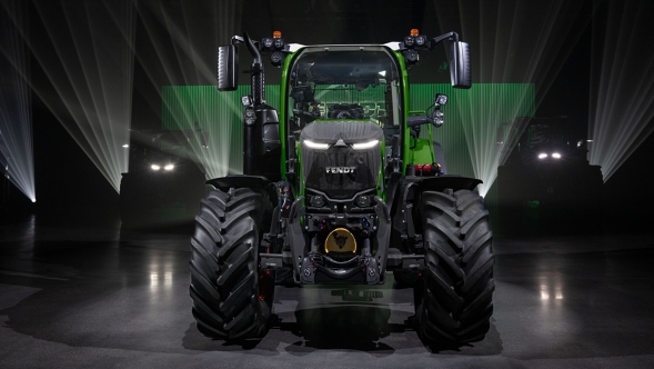 Ein Fendt 300 Vario Gen5 Traktor steht frontal im Rampenlicht in einer dunklen Halle mit Lichtstrahlen und betonter grüner LED-Beleuchtung
