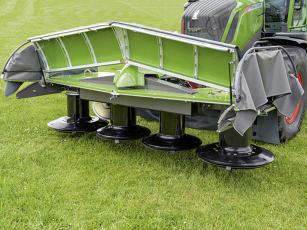 Nahaufnahme eines grünen Fendt Frontmähwerks mit vier schwarzen Mähscheiben auf grünem Gras. Die Schnitthöhe ist manuell einstellbar über eine robuste, verschleißfeste Trommelschlittenmechanik. Graue Schutzabdeckungen sind seitlich zu sehen.