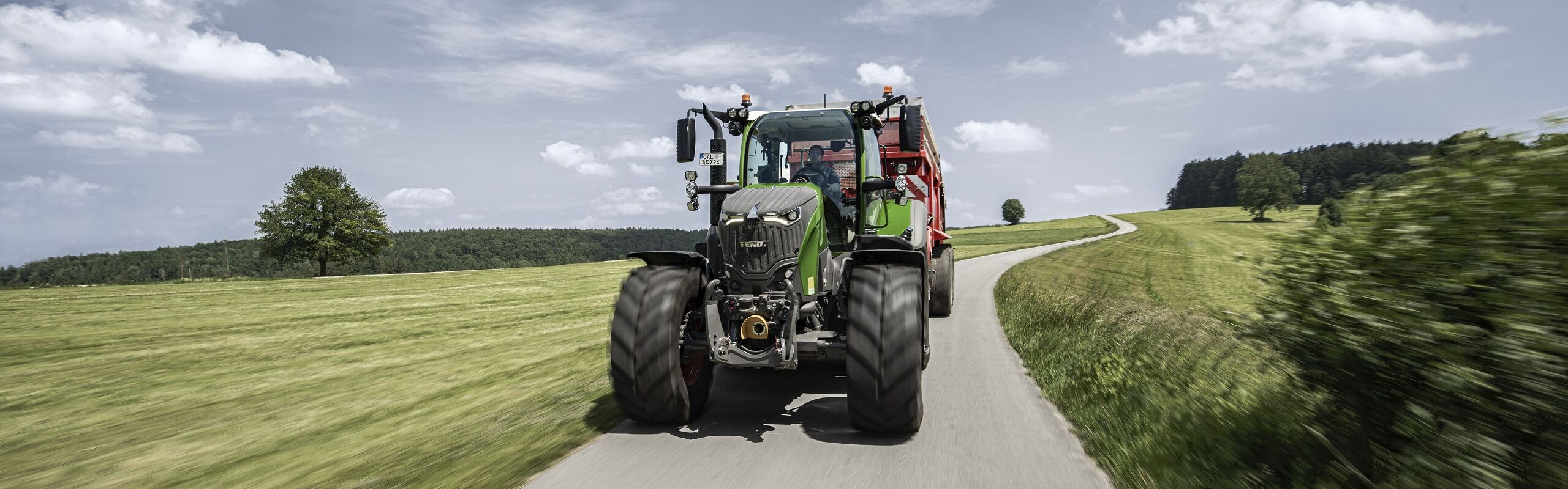 Ein Fendt 700 Vario mit Ladewagen fährt im Sommer auf einer Landstraße