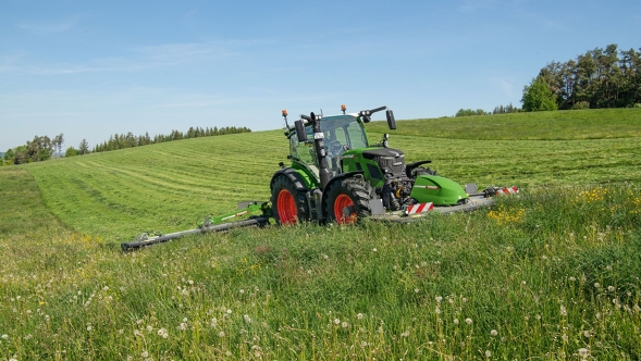 Fendt 500 Vario Gen4 mit Mähwerk beim Mähen einer hügeligen Grünfläche an einem sonnigen Tag