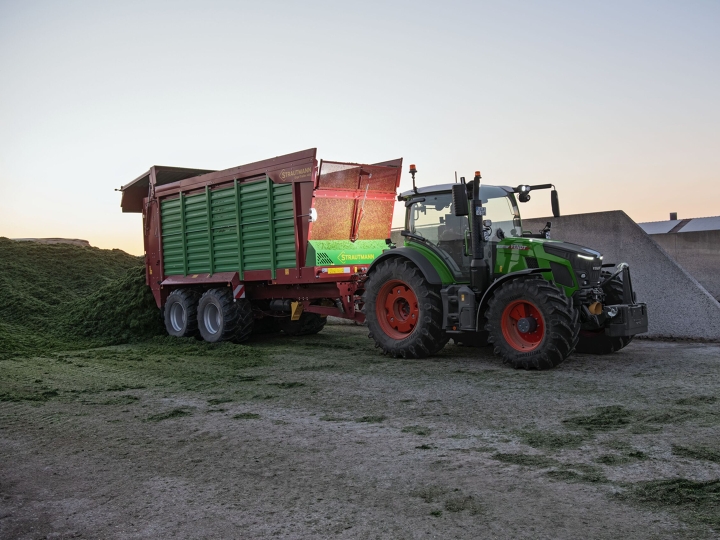 Fendt 500 Vario Gen4 beim Entladen eines Ladewagens bei Dämmerung auf dem Feld