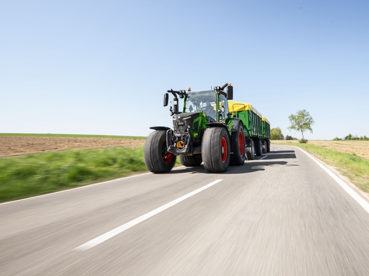 Fendt 500 Vario Gen4 fährt mit einem Anhänger auf Landstraße bei sonnigem Wetter