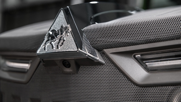 Nahaufnahme der silberfarbenen Haubenkamera auf der Motorhaube eines Fendt 500 Vario Gen4 Traktors. Die Kamera ist unter dem markanten Fendt-Dreieck-Emblem montiert, das in glänzendem Silber auf schwarzem Untergrund hervorsticht. Die Motorhaube ist dunkelgrau mit strukturiertem Muster, flankiert von zwei modernen LED-Scheinwerfern.