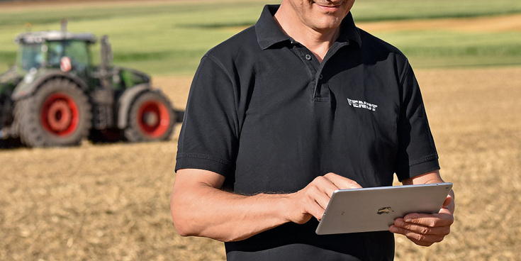 Mann mit Tablett auf Acker und Fendt im Hintegrund