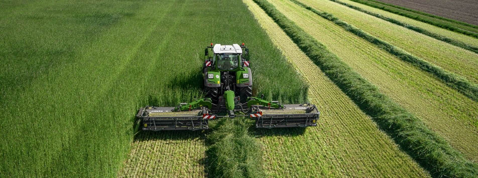 Ein Fendt Traktor mit Fendt Slicer Mähwerk auf einer grünen Wiese aus der Vogelperspektive.