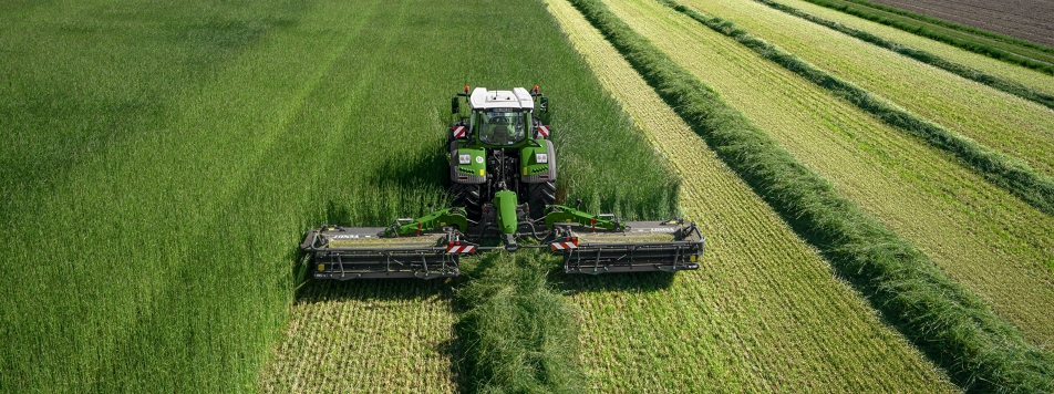 Ein Fendt Traktor mit Fendt Slicer 960 KCB Pro Mähkombination auf einer Wiese beim Mähen aus der Vogelperspektive.