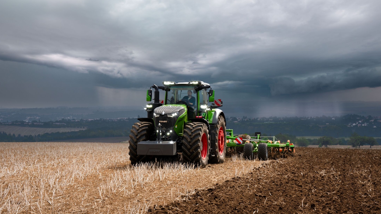 Vor schweren, heraufziehenden Gewitterwolken in der Ferne erledigt der Fendt 1000 Vario Traktor noch kraftvoll seine Feldarbeit