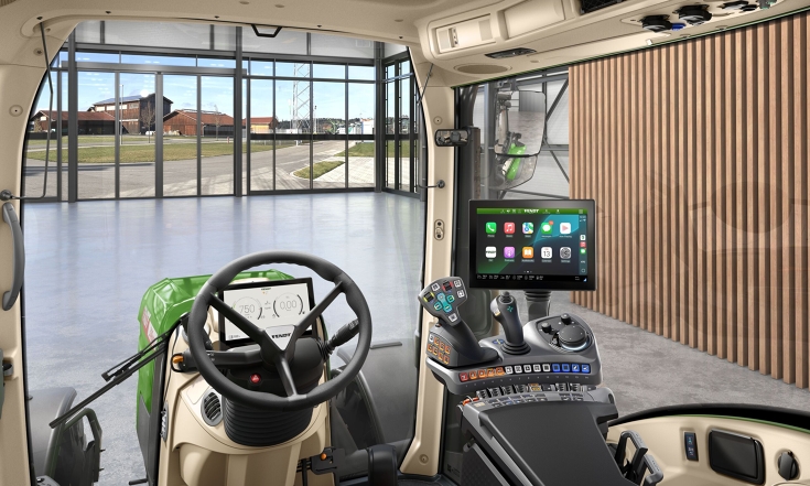 Innenraum der Fendt Kabine mit Apple CarPlay Eine Innenaufnahme der Traktorkabine aus Sicht des Fahrers mit Lenkrad, FendtONE Bedienarmlehne mit Joystick und Apple CarPlay auf dem Terminal sowie einen zusätzlichen Terminal im Dach.
