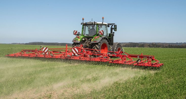 Ein Fendt 300 Vario mit einem Striegel im Grünland Ein grüner Fendt 300 Vario fährt mit einem roten Striegel über das Grünland.
