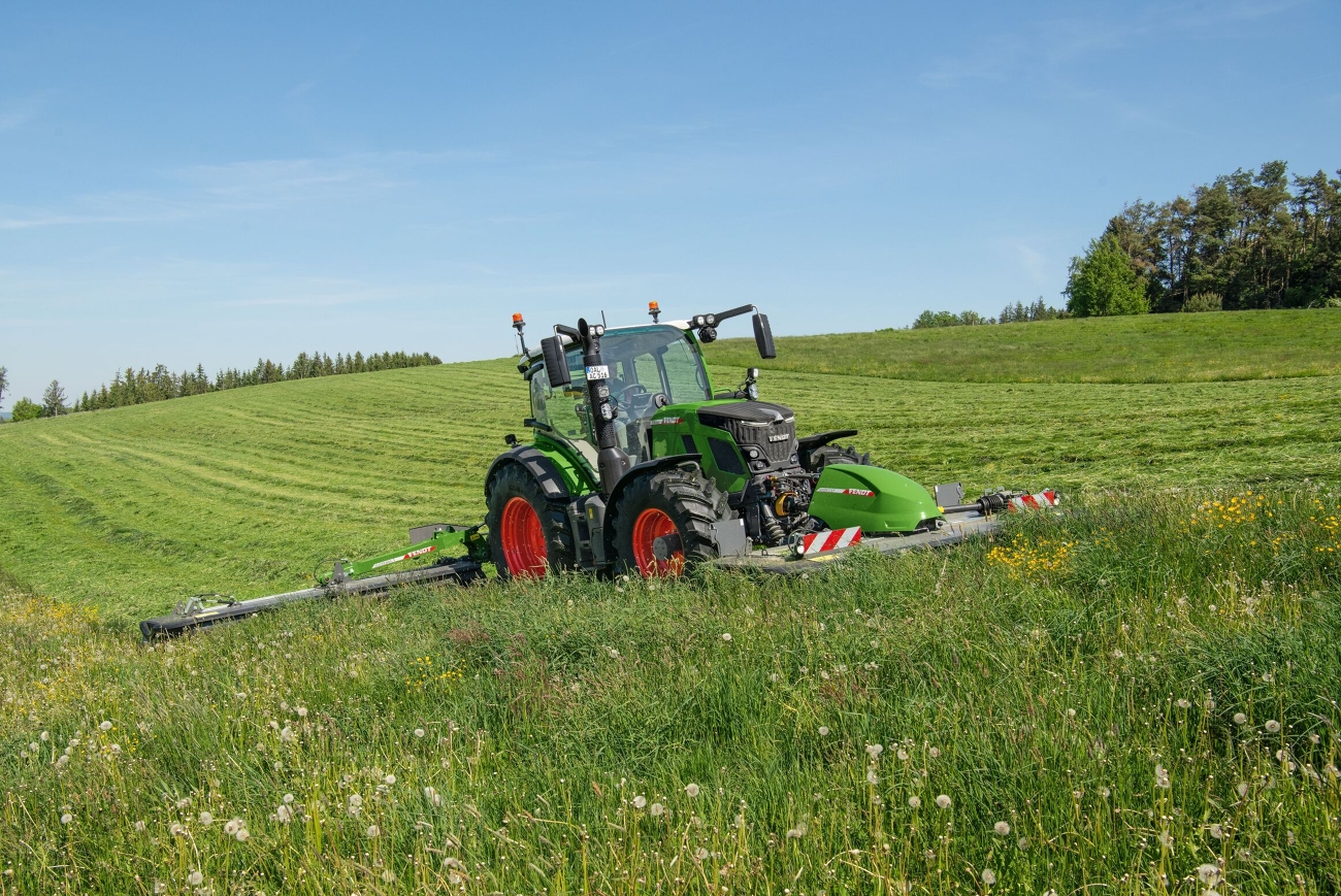 Ein grüner Fendt 500 Vario mäht eine Grünfläche mit einem Front- und einem Heckmähwerk.