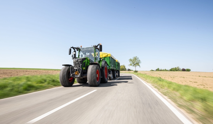 Ein Fendt 500 Vario mit zwei Anhängern im Straßentransport Ein grüner Fendt 500 Vario fährt mit zwei grünen Anhängern mit einer gelben Folienabdeckung über eine Straße.