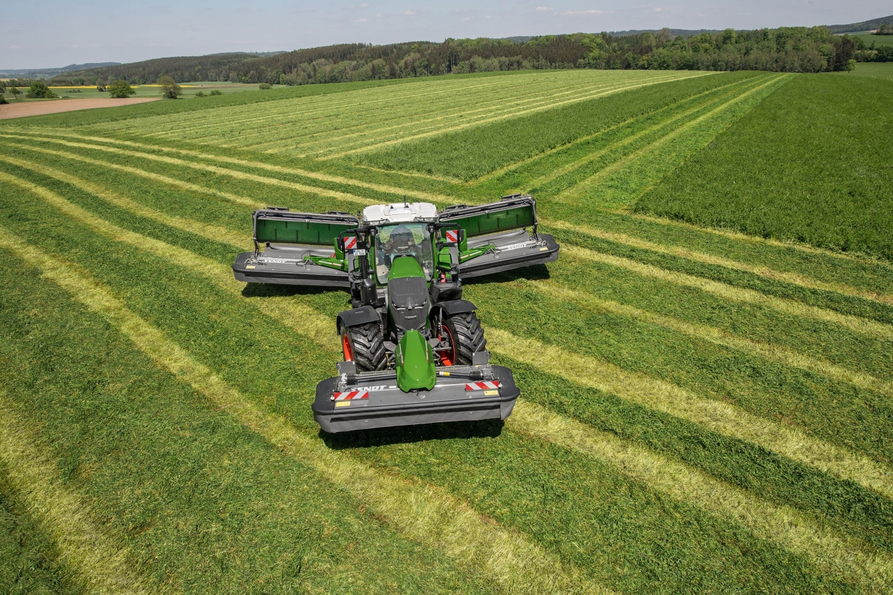 Ein grüner Fendt 800 Vario wendet mit angehobenen Mähwerken auf dem Grünland.