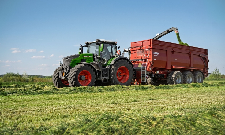 Ein Fendt 800 Vario fährt in der Häckselkette Eine grüner Fendt 800 Vario fährt neben einem Häcksler während dieser den roten Anhänger von Krampe füllt.