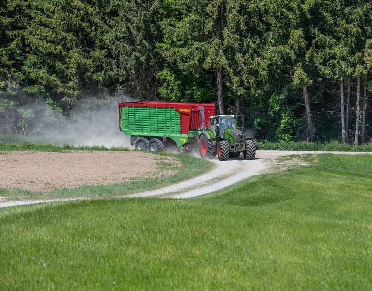 Ein Fendt 724 Vario Gen7.1 transportiert einen Strautmann Ladewagen Ein grüner Fendt 724 Vario Gen7.1 fährt im Gespann mit einem Strautmann Ladewagen über einen Feldweg. Im Hintergrund ist ein Wald zu sehen.