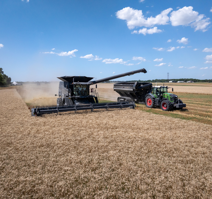 Fendt IDEAL neben einem Fendt Traktor mit OutRun im Gespann mit einem Überladewagen Ein schwarzen Fendt IDEAL tankt in einen schwarzen Überladewagen ab, der von einem autonom fahrenden grünen Fendt Traktor gezogen wird