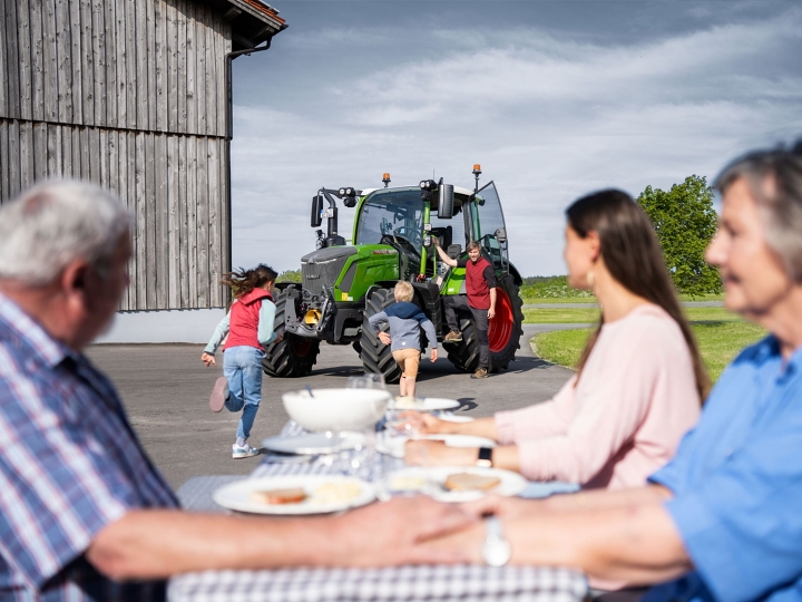 Kampagnenmotiv zum Fendt 300 Vario Gen5 Am gedeckten Tisch sitzt die Familie auf ihrem Hof und freut sich über die Ankunft der letzten zwei Familienmitglieder: Landwirt und Fendt 300 Vario