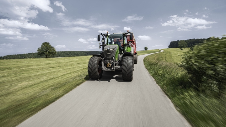 Kampagnenbild zum Fendt 700 Vario Gen7.1 Ein grüner Fendt 700 Vario Gen7.1 fährt auf einer Landstraße im Sommer zwischen grünen Feldern links und rechts