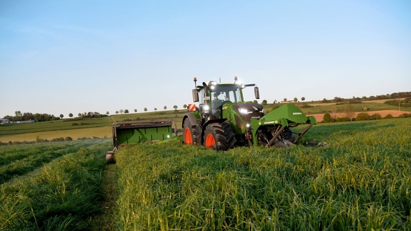 Fendt Traktor mit Slicer-Kombination beim mähen einer grünen Wiese mit blauen Himmel
