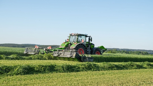 Fendt Traktor mit Slicer-Heckmähwerk beim mähen auf einer grünen Wiese mit blauem Himmel
