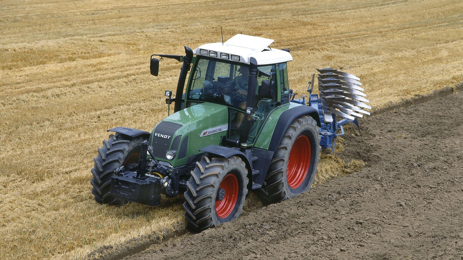 Ein grüner Fendt Favorit 700 Vario pflügt ein Feld, das zur Hälfte mit goldenen Stoppeln bedeckt und zur Hälfte frisch umgegraben ist.
