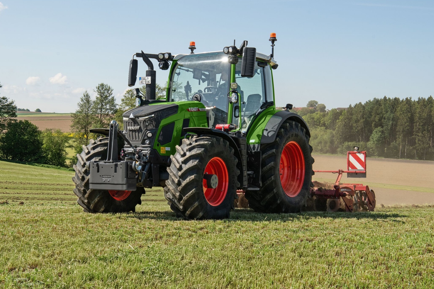 Fendt 500 Vario Traktor auf dem Feld Der Fendt 500 Vario Gen4 in grün mit roten Felgen bei der Bodenbearbeitung auf der Wiese mit einer roten Scheibenegge