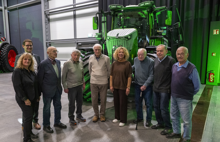 Eine Gruppe von Menschen steht vor einem grünen Traktor in einem Ausstellungsraum.