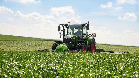 Fendt 600 Vario bei der Grünlandbearbeitung auf dem Feld Ein Fendt 600 Vario mit angebautem Arbeitsgerät bei der Bearbeitung eines grünen Feldes unter blauem Himmel
