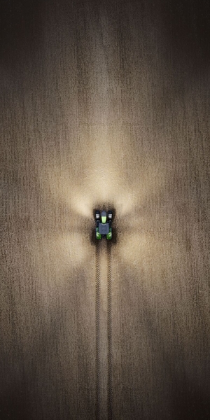 Ein Fendt Traktor fährt bei Dunkleheit über den Acker und man sieht den Traktor aus der Vogelperspektive und somit sein Dach und wie er mit Licht den Acker ausleuchtet.