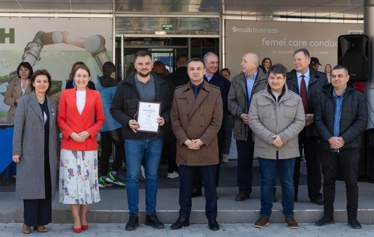 Fendt MOMENTUM 16 in Moldau ausgezeichnet Eine Gruppe von Menschen steht vor einem Gebäude; ein Mann hält eine Urkunde in der Hand.