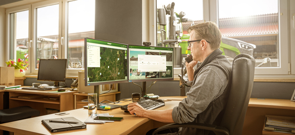 En entreprenør sidder ved sit skrivebord foran to skærme og taler i telefon.