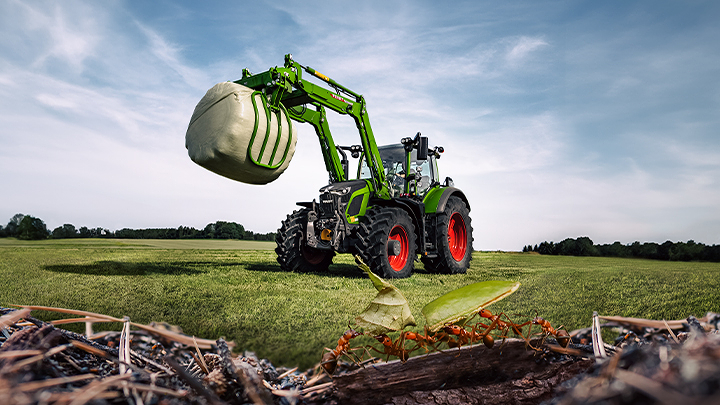 En Fendt 600 Vario-traktor står på marken og løfter en siloballe. Myrer kan ses i forgrunden.