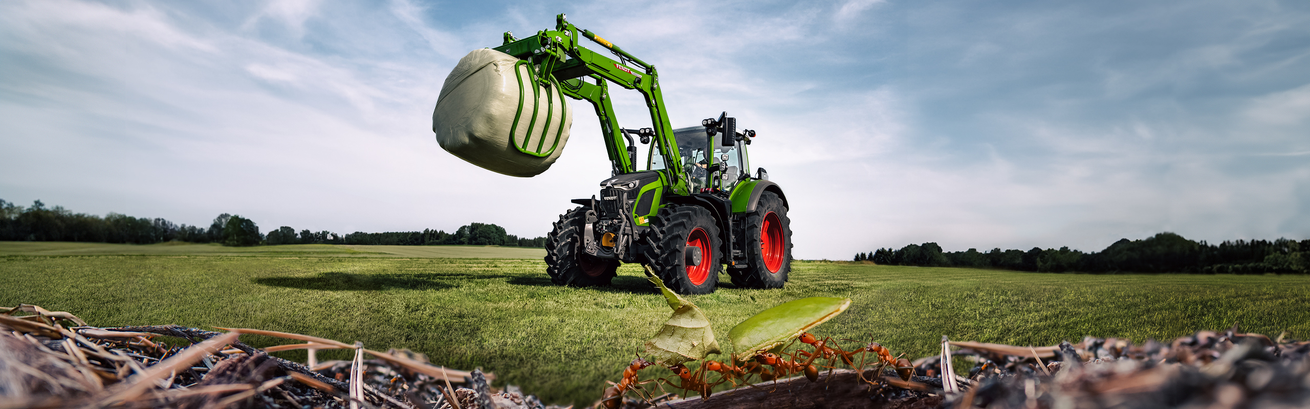 En Fendt 600 Vario-traktor står på marken og løfter en siloballe. Man kan se myrer i forgrunden.