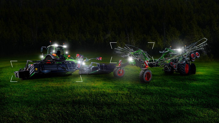 To traktorer med en Fendt Slicer slåmaskine og en Fendt Former rive står i dæmringen på en mark og blive belyst.