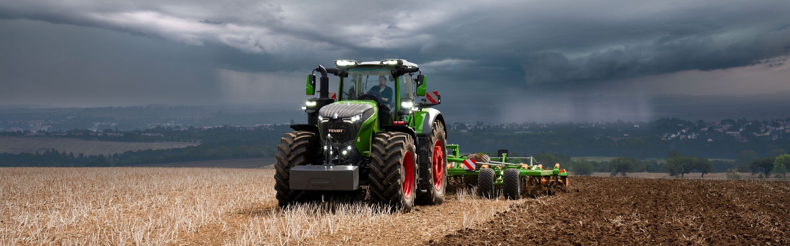 Med de tunge tordenskyer i det fjerne, klarer Fendt 1000 Vario traktoren sit arbejde i marken med rigelige kræfter.
