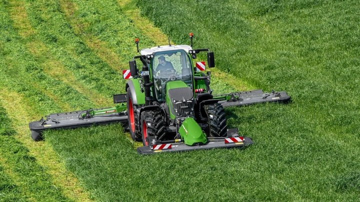Den grønne Fendt 600 Vario traktor slår med det grønne redskab Fendt Slicer græs på en grøn eng, i baggrunden ses slåspor.