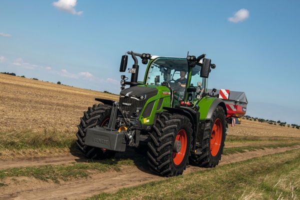 Fendt 600 Vario Den grønne Fendt 600 Vario traktor med røde fælge kører på en smal markvej med en lyseblå himmel i baggrunden.