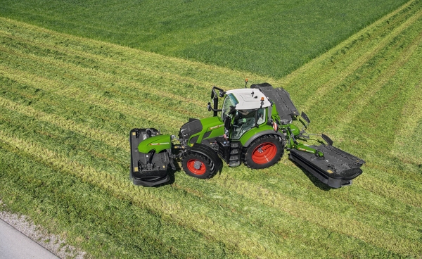 Den grønne traktor Fendt 600 Vario ved arbejdet med slåmaskinen Fendt Slicer arbejder på en stor, grøn eng, set fra fugleperspektivet.