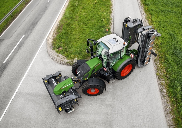 Den grønne traktor Fendt 600 Vario med røde fælge og redskabet vippet ind kører med en lille venderadius på en grå vej.