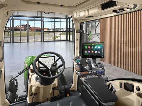 Una vista interior de la cabina del tractor desde la perspectiva del conductor con volante, reposabrazos de control FendtONE con joystick y Apple CarPlay en el terminal, así como un terminal adicional en el techo.