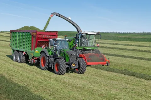 Un Fendt 724 Vario Gen7.1 verde circula con un remolque autocargador Strautmann junto a una picadora de forraje Fendt Katana verde que corta hierba.