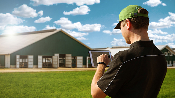 Un agricultor con una tablet se encuentra frente a su granja y se inscribe a la newsletter