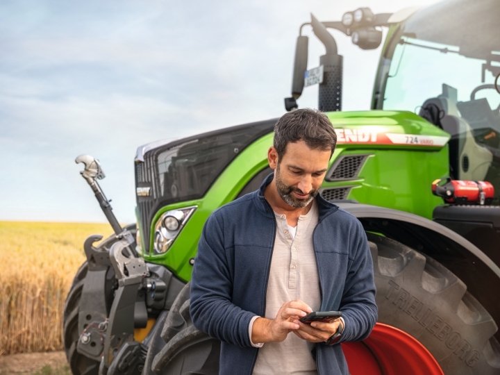 Un agricultor de pie, al lado de un su tractor Fendt 724 mirando su teléfono móvil