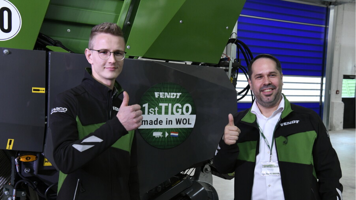 Dos empleados de Fendt están delante de un Fendt Tigo y levantan el pulgar derecho. En el Tigo hay pegada una pegatina con el texto «1er Tigo fabricado en WOL».