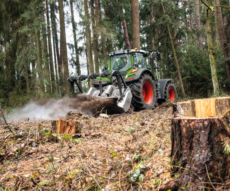 Fendt 700 Vario Gen7 con fresadora en la parte trasera Un Fendt 700 Vario Gen7 corta troncos en un bosque de coníferas.