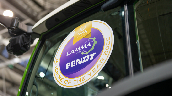 Primer plano de la luna de parabrisas del tractor desde delante con una pegatina redonda grande «Machine of the Year 2025» en azul y dorado en la LAMMA 2025.