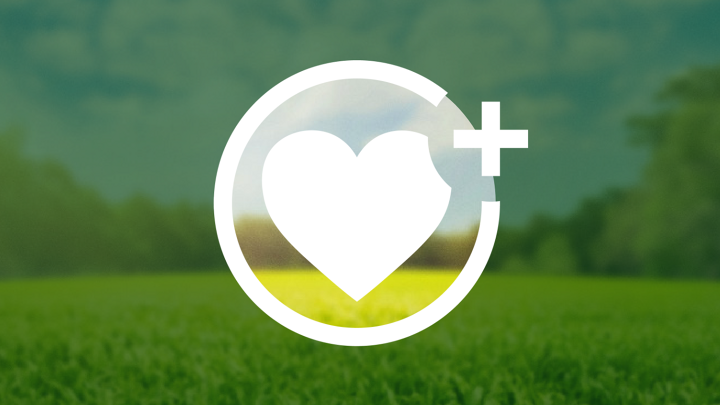 Un corazón blanco está dentro de un círculo con un signo más a la derecha. El fondo muestra una pradera forestal verde bajo un cielo azul, oscurecido fuera del círculo por una capa verde oscura, parcialmente transparente.