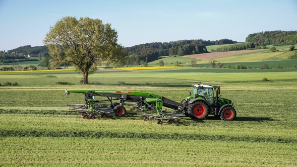 Fendt Former 14055 PRO Un tractor Fendt verde con llantas rojas y Fendt Former 14055 PRO enganchado gavillando en una pradera verde estival