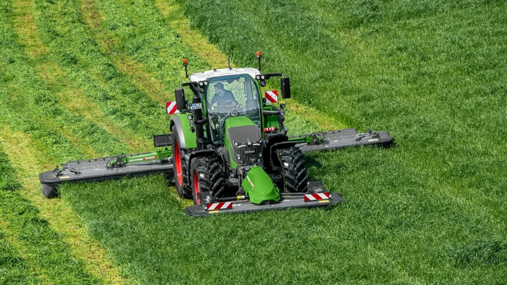 El tractor Fendt 600 Vario verde siega con un implemento verde, el Fendt Slicer, un prado verde; al fondo se ven las huellas de la siega.