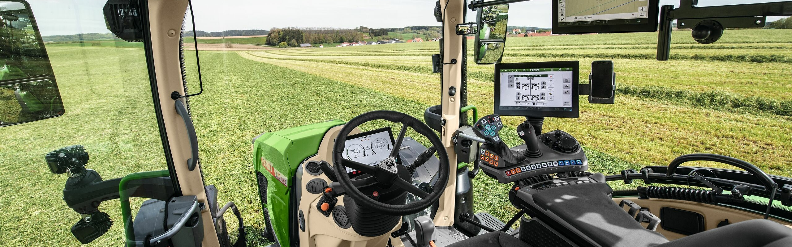Vista interior de la cabina del Fendt 600 Vario con vistas a un prado verde.